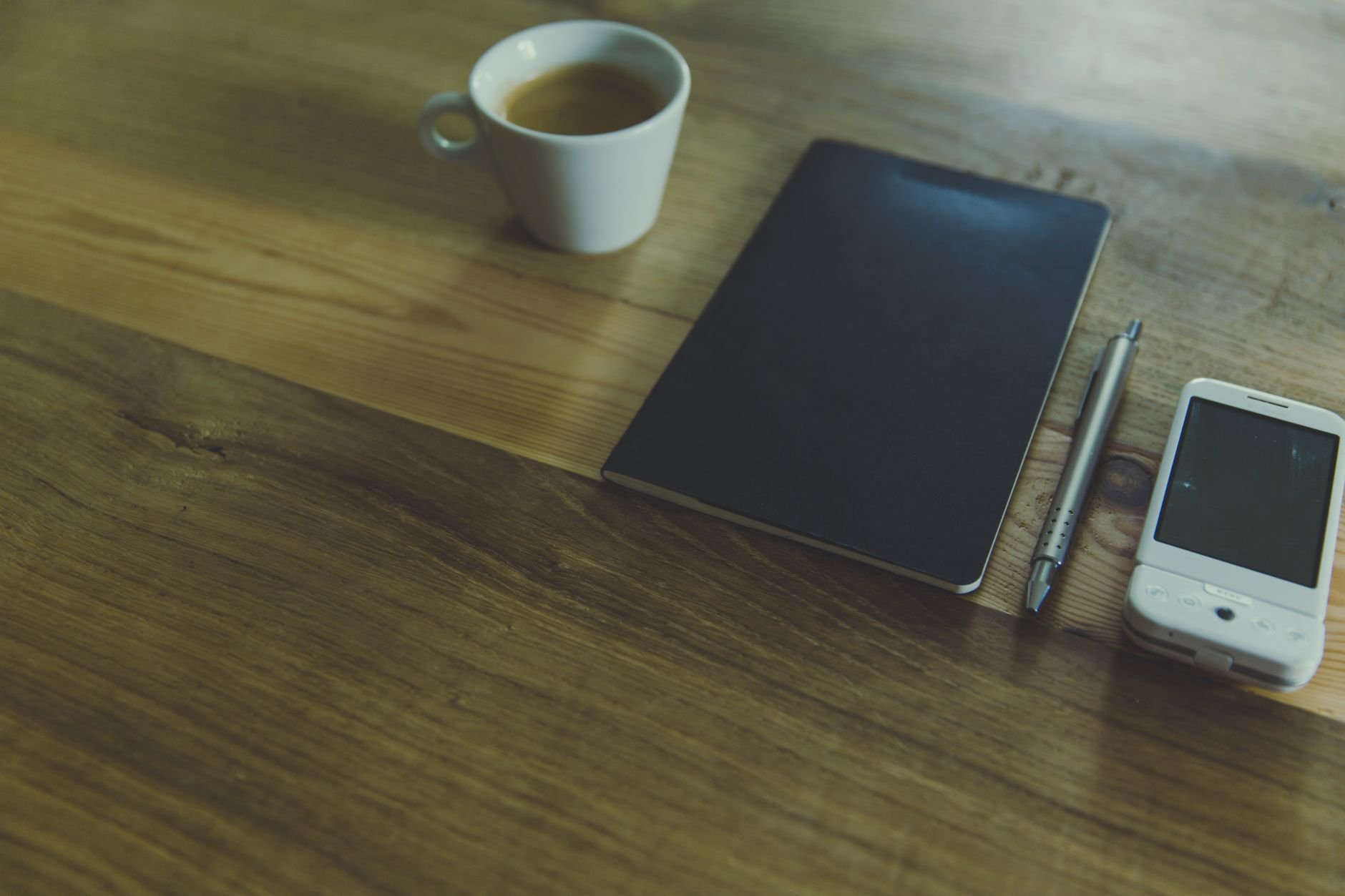 A simple workspace setup featuring a coffee cup, notebook, and pen on a wooden desk